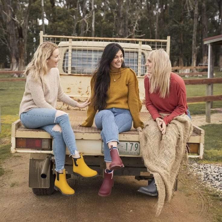 minimalist vegan, 3 women sitting on the back of a farm truck wearing merry people boots