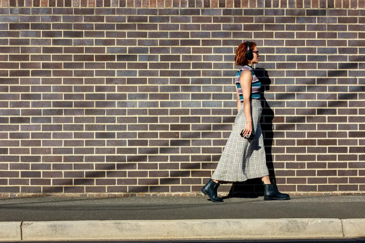 Red headed woman wearing Merry People boots, walking down the street and listening to podcasts